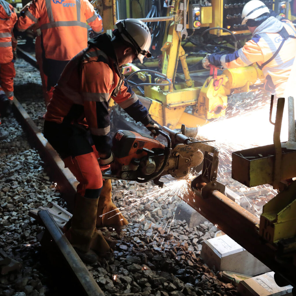 Ouvrier sur un chantier de changement de rail en train de couper un reil de train.